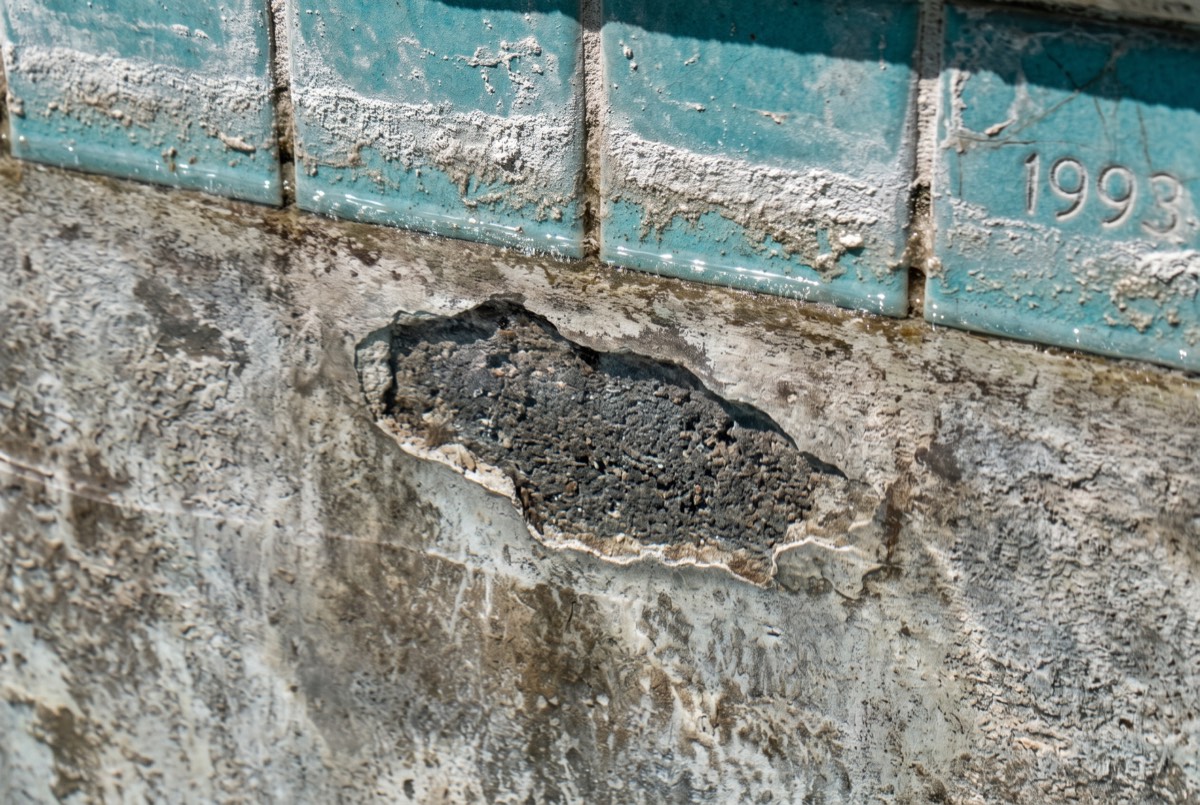 Failing pool plaster with stains and exposed gunite below dated 1990s teal waterline tile